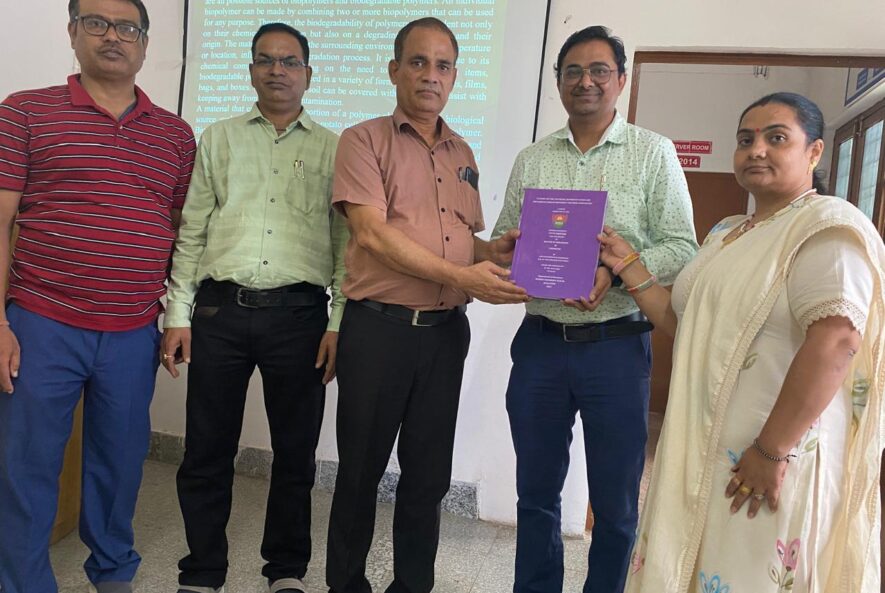 Group of five people posing indoors during a thesis presentation, one person holding a purple bound thesis