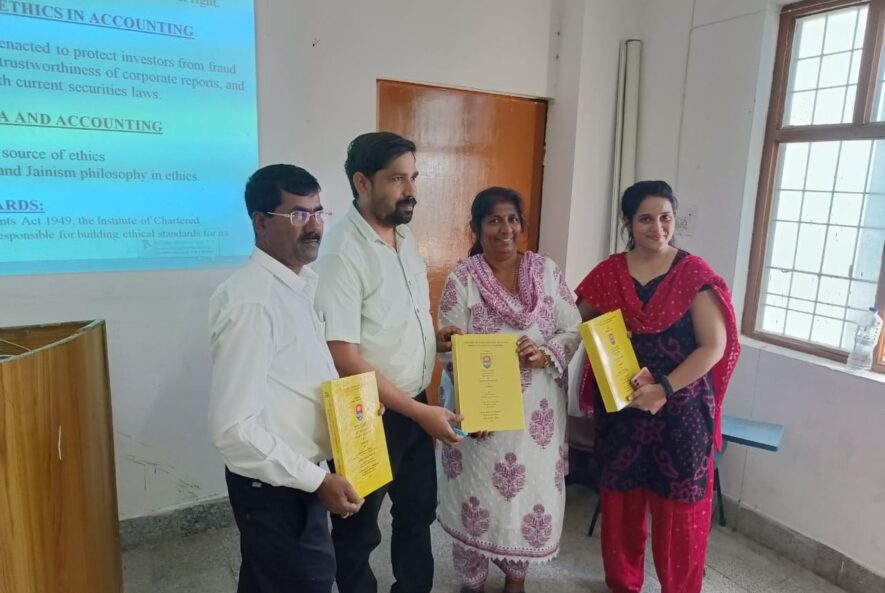Group of four people holding yellow bound theses at a presentation ceremony in a classroom