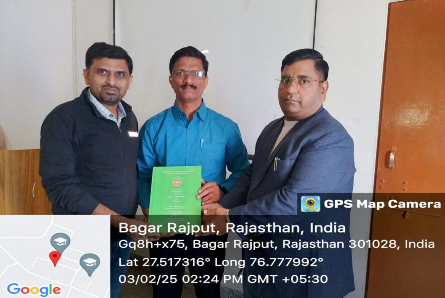 Three men posing indoors with a green bound thesis during a submission ceremony in Bagar Rajput, Rajasthan