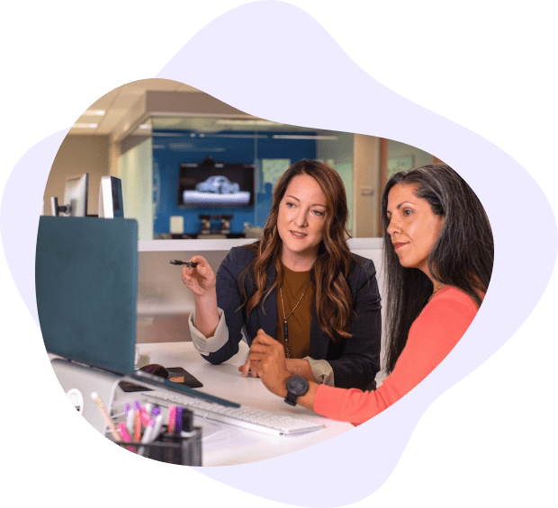 Two women discussing business strategy while working on a computer in an office